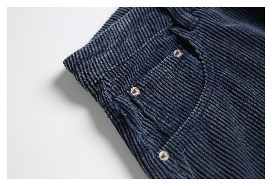 Close-up of a curved front pocket and metal rivets on navy ribbed trousers.