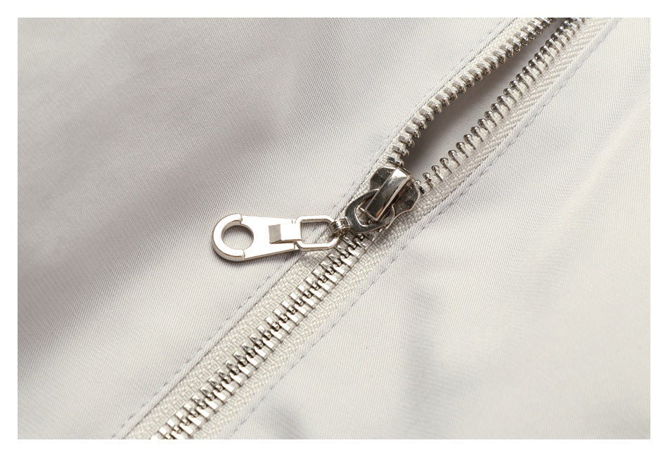 Close-up of a silver metal zipper and pull on light gray fabric.