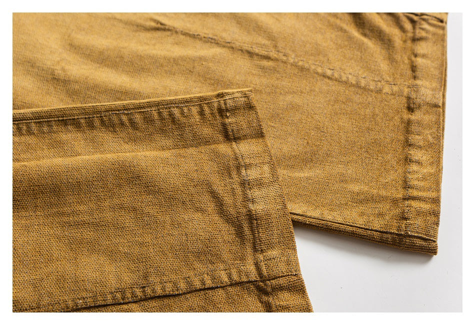 Close-up of mustard-brown pants showing a patch pocket, stitching, and finished leg hem.