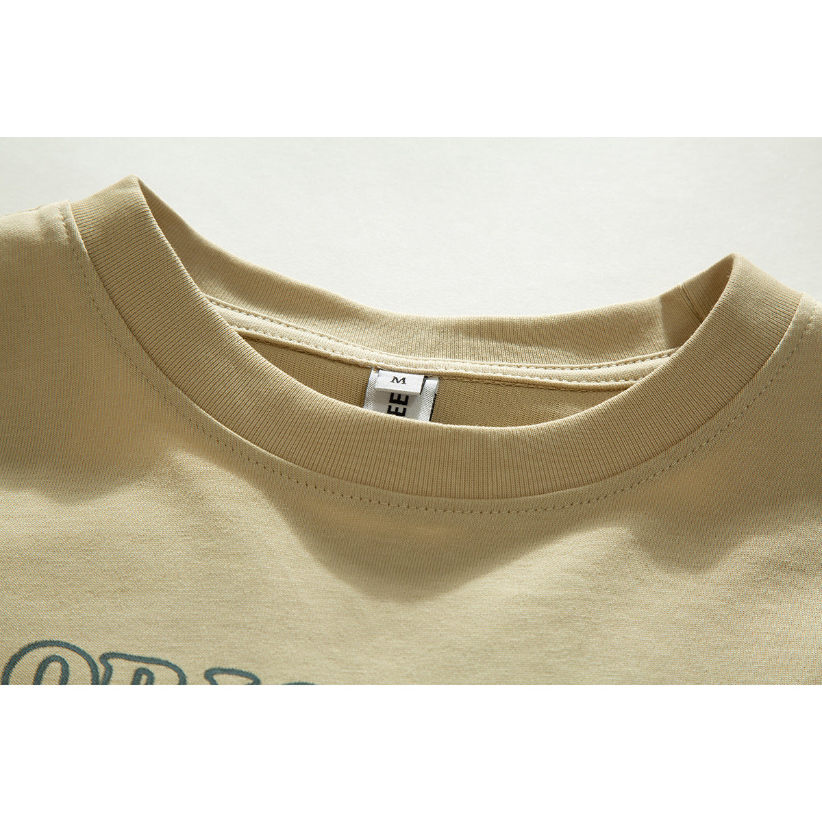 Close-up of a beige T-shirt's ribbed crew neck, size label, and partial dark printed graphic.