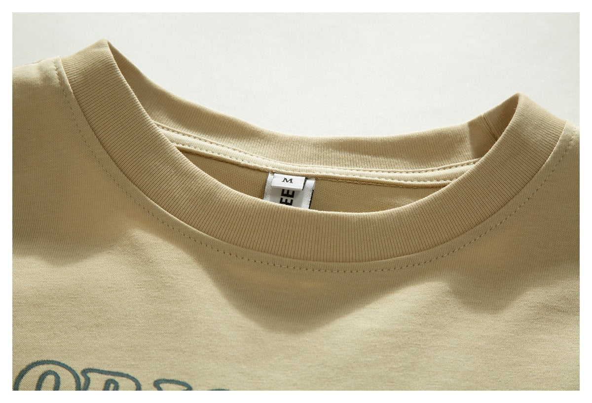 Close-up of a beige T-shirt's ribbed crew neck, size label, stitching, and partial printed graphic.