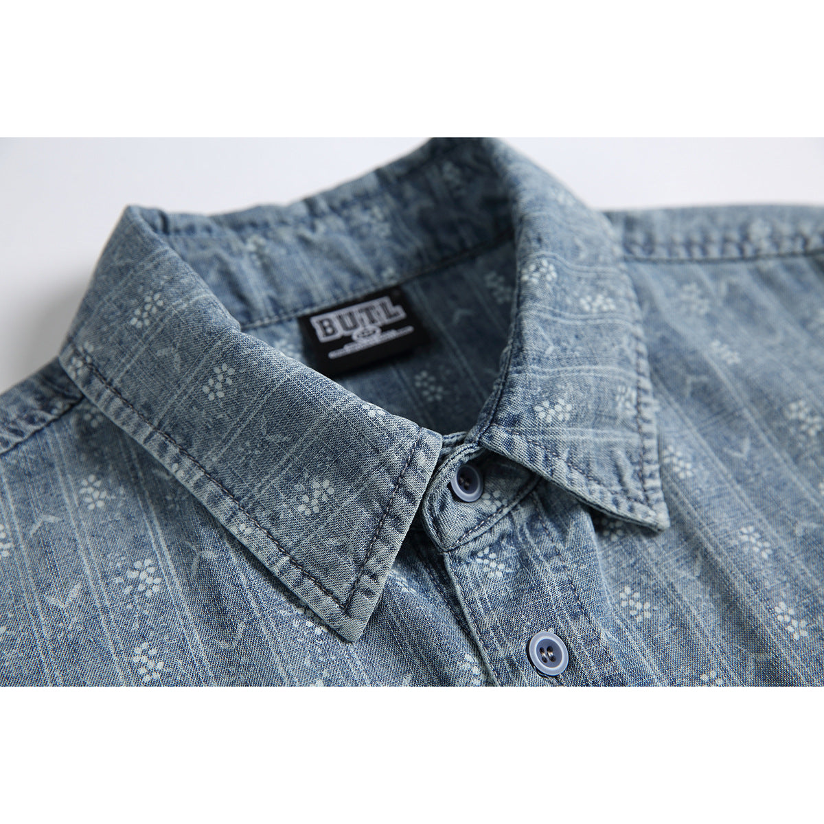 Close-up of a blue-gray patterned shirt collar, buttons, and sewn neck label.