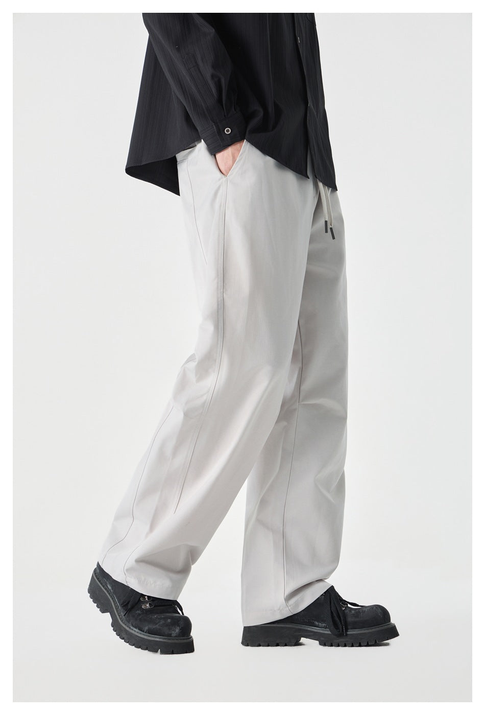 Side view of a cropped model wearing light gray wide-leg drawstring pants with a black shirt and shoes.