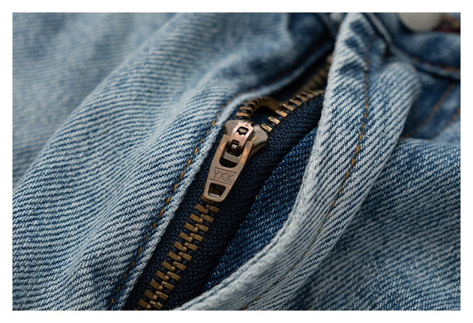 Close-up of a brass zipper and pull on light blue jeans; YKK is stamped on the pull.