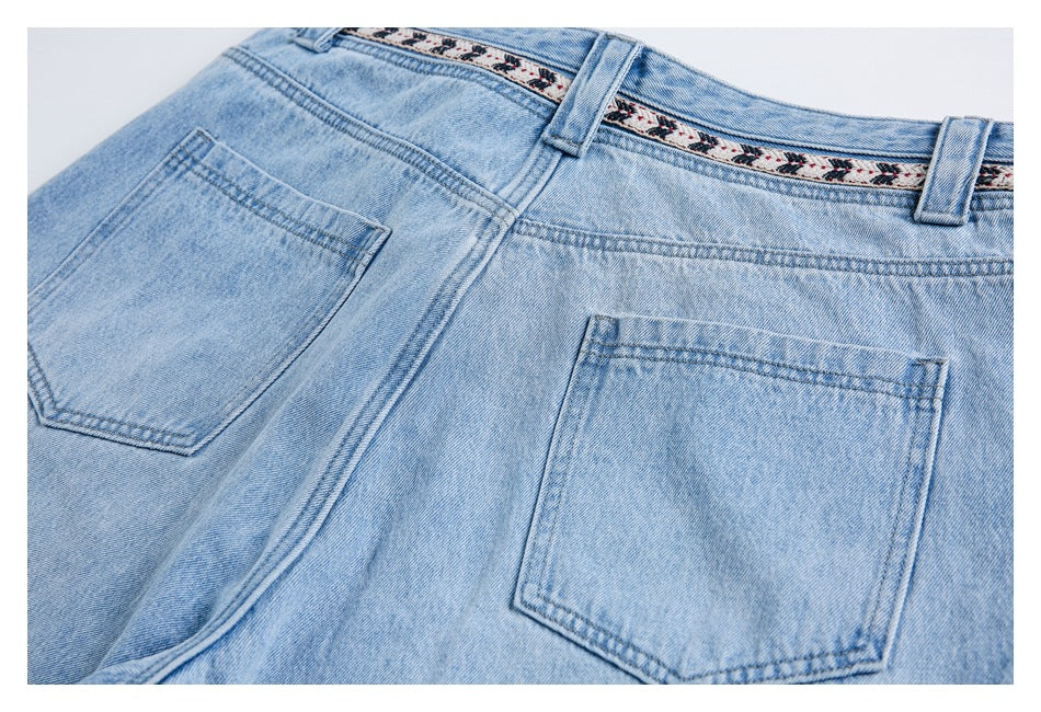 Close view of the back of light-wash jeans, showing two pockets, belt loops and patterned waistband trim.