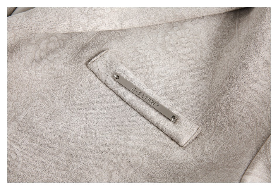 Close-up of a pale beige paisley blazer pocket with a narrow metal logo tab.