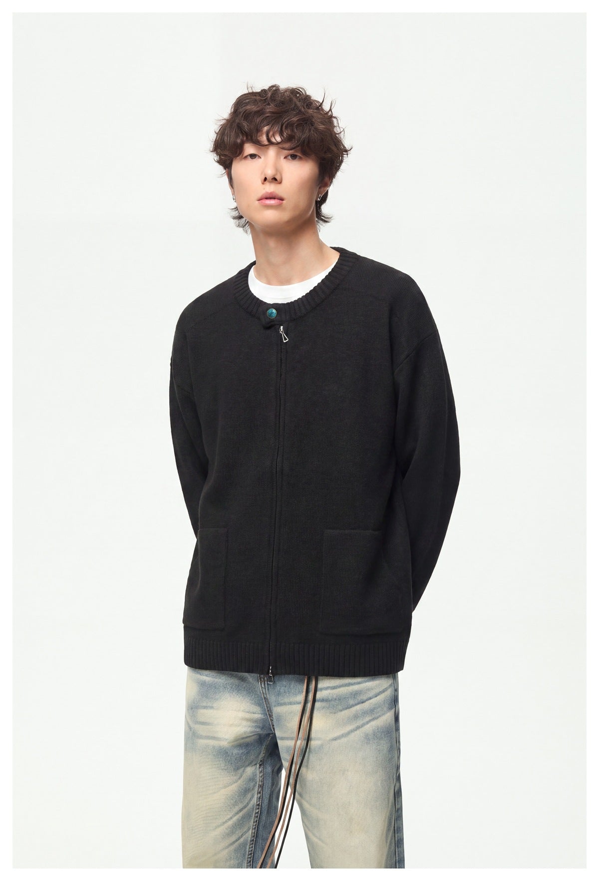 Model wearing a black knit cardigan zipped up, with a ribbed crew neck, contrast button and two patch pockets.