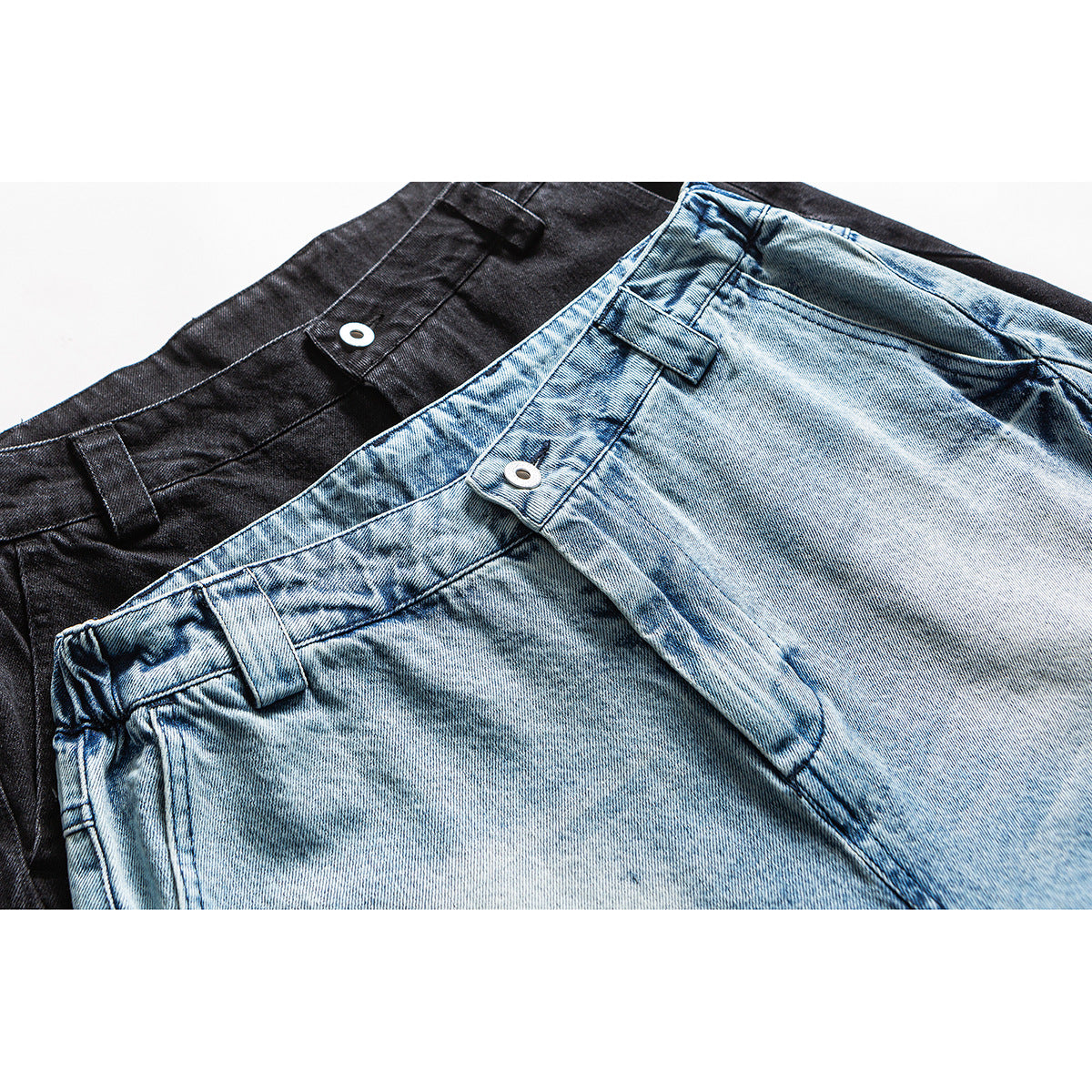Close-up of light blue and black jeans showing the waistbands, belt loops and metal buttons.