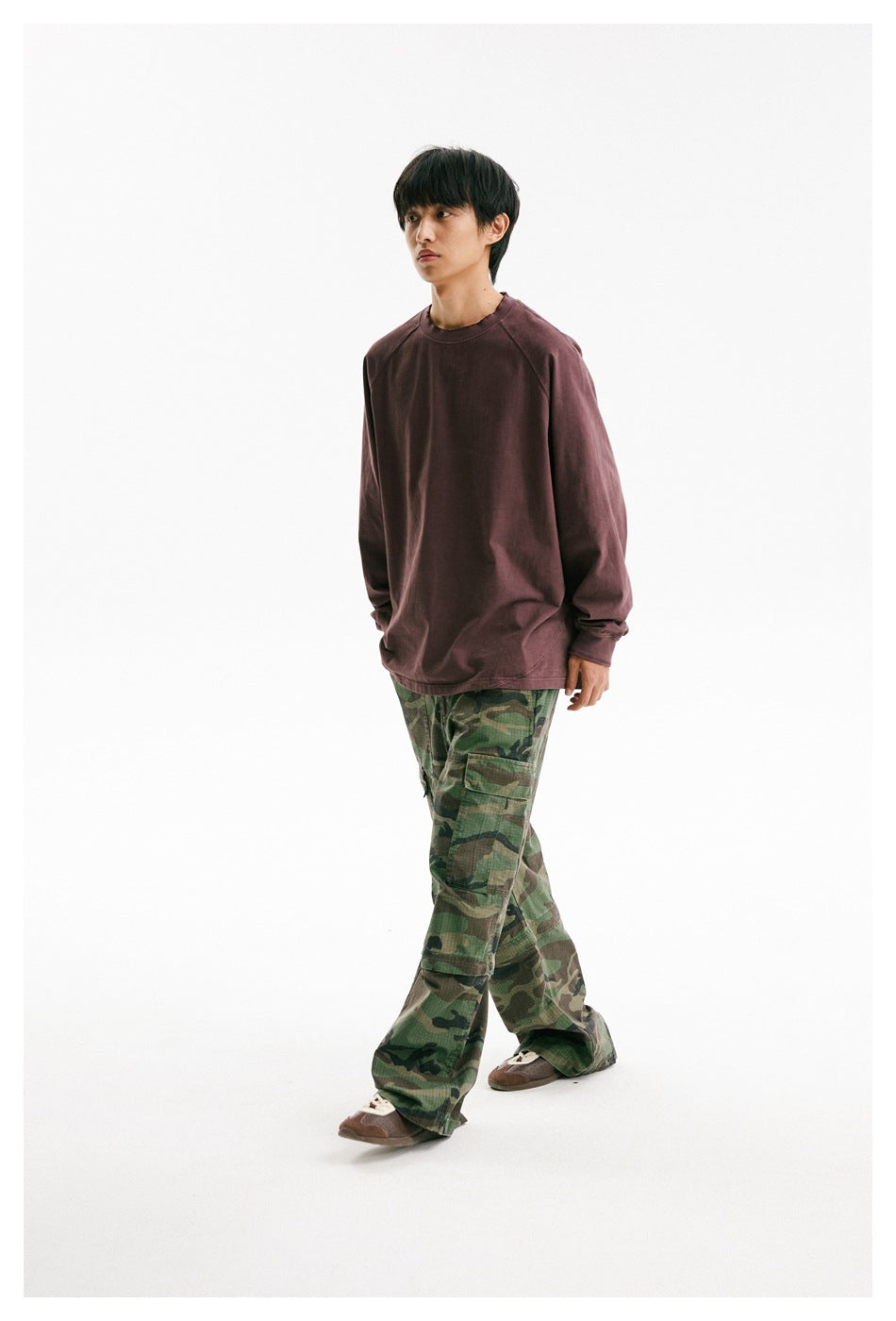 Male model walking in a loose muted-plum long-sleeve shirt and green camouflage cargo pants.