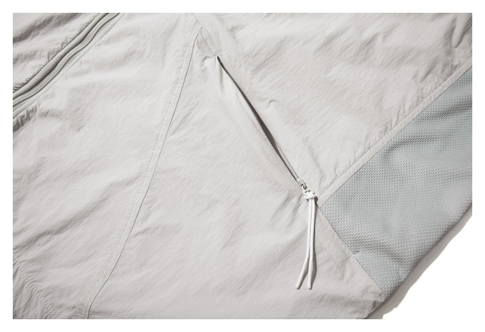 Close-up of the light gray jacket's side zipper with a long drawcord pull beside a mesh panel.