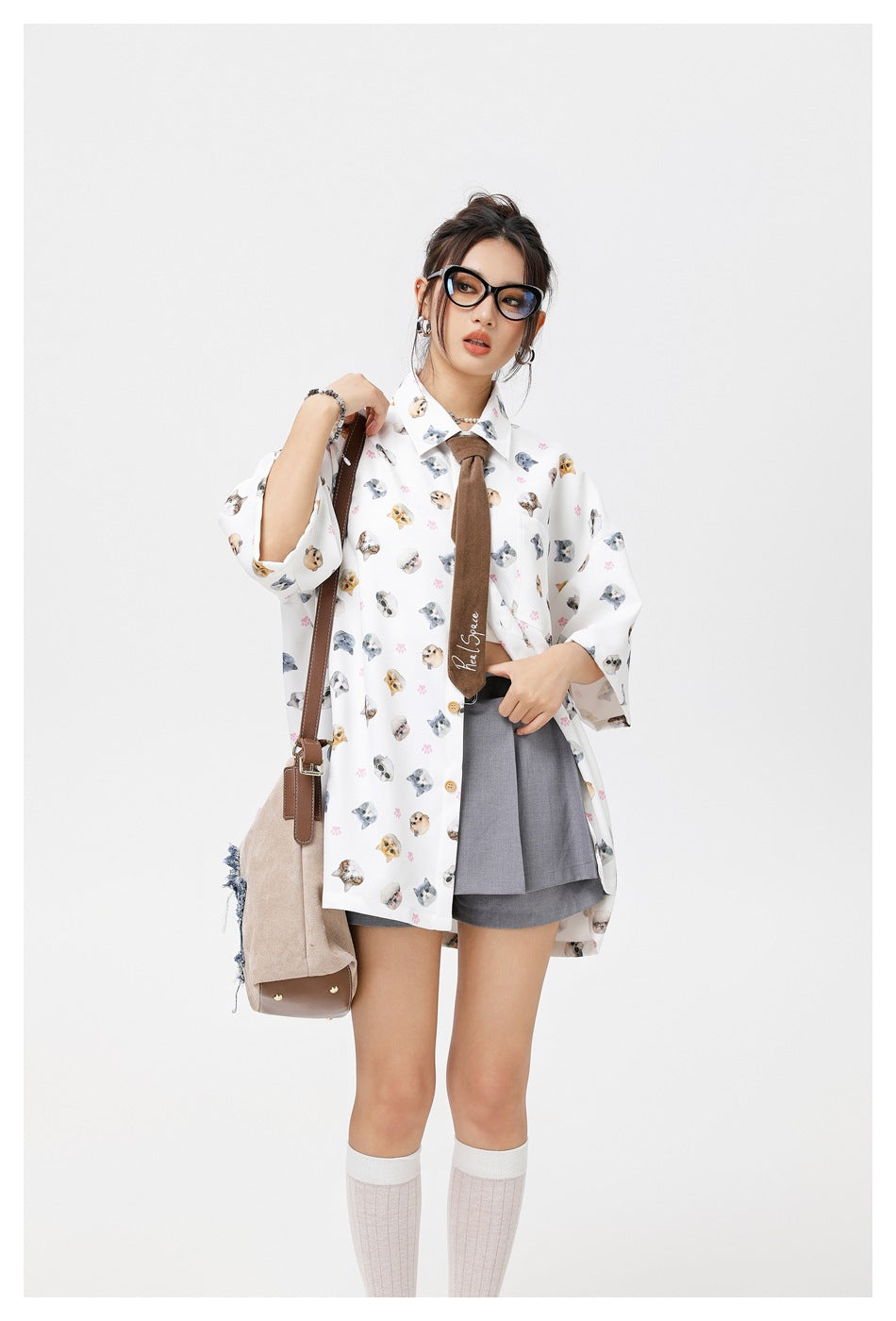 Closer view of a model in a white cat-print shirt and brown tie, with a gray skirt visible underneath.