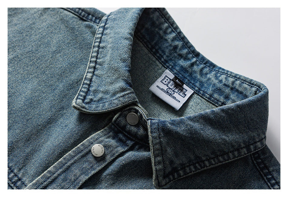 Close-up of a washed blue denim collar, metal button and sewn neck label.