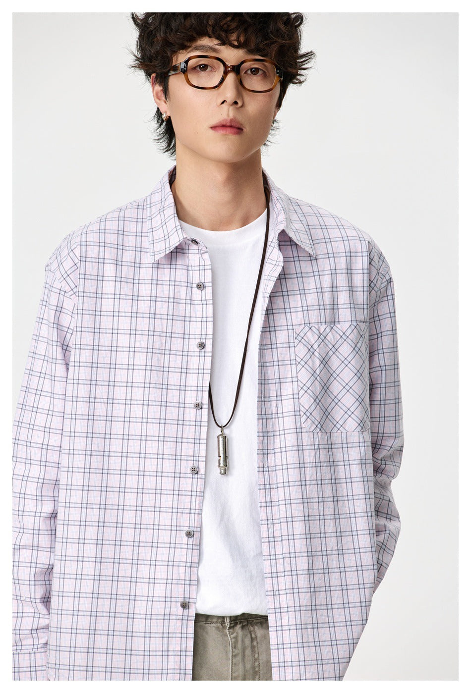 Front close-up of a model wearing an open pale pink plaid shirt with a contrasting angled-plaid chest pocket.
