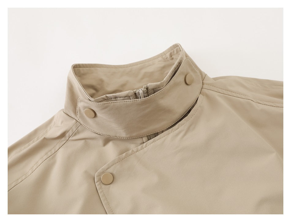 Close-up of a beige jacket's high collar, zipper, and snap-button front closure.
