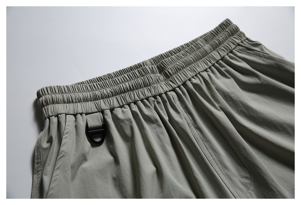 Close-up of the gray-green shorts' elastic waistband, front pockets, and small black loop.