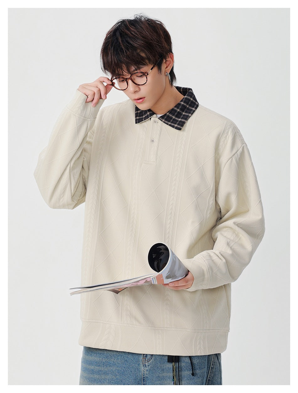Model wearing an ivory pullover with a dark plaid collar, adjusting his glasses while holding an open magazine.
