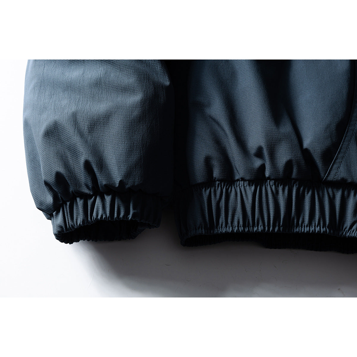 Close-up of a dark jacket sleeve and lower edge, both finished with gathered elastic cuffs.