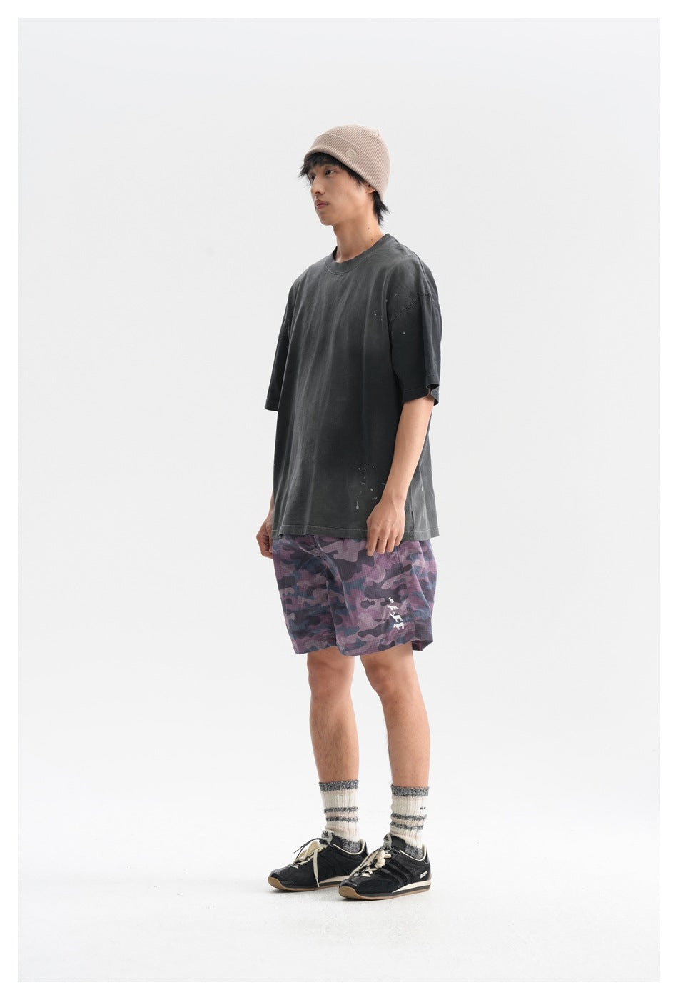 Person wearing a faded black oversized T-shirt with camouflage shorts and a beanie, side view