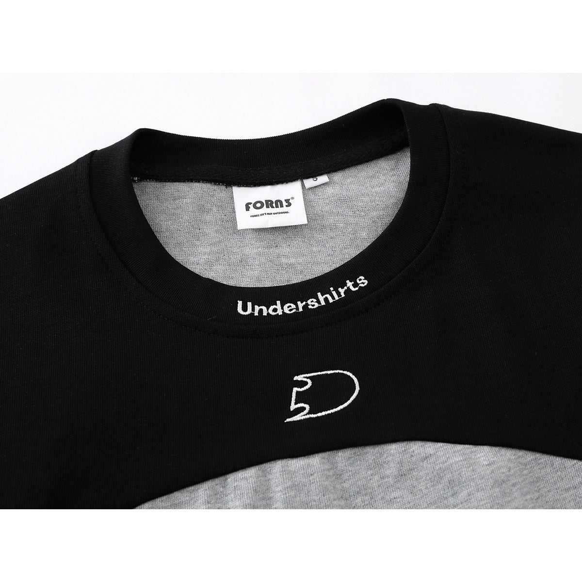 Close-up of a black crew neck and chest with white embroidered lettering and emblem on a gray color-block shirt.