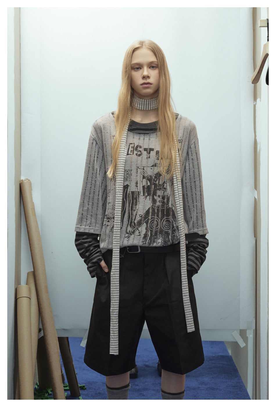 Front view of a model wearing a gray graphic T-shirt over a dark striped long-sleeve top and black wide-leg shorts.