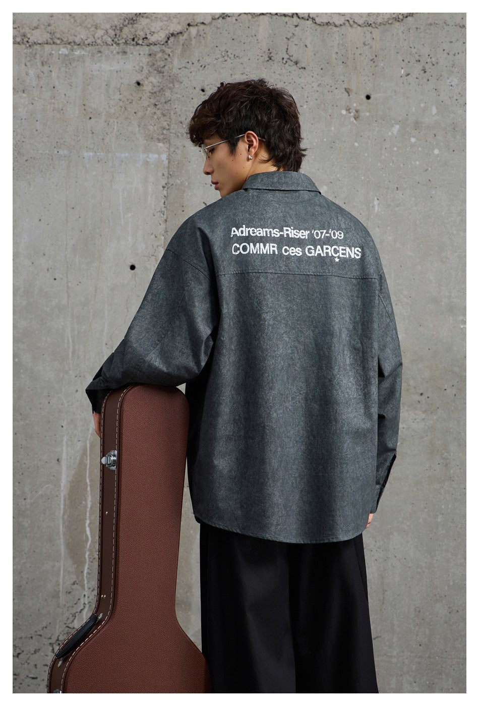 Back view of a model wearing a charcoal gray oversized shirt with large white text across the shoulders.