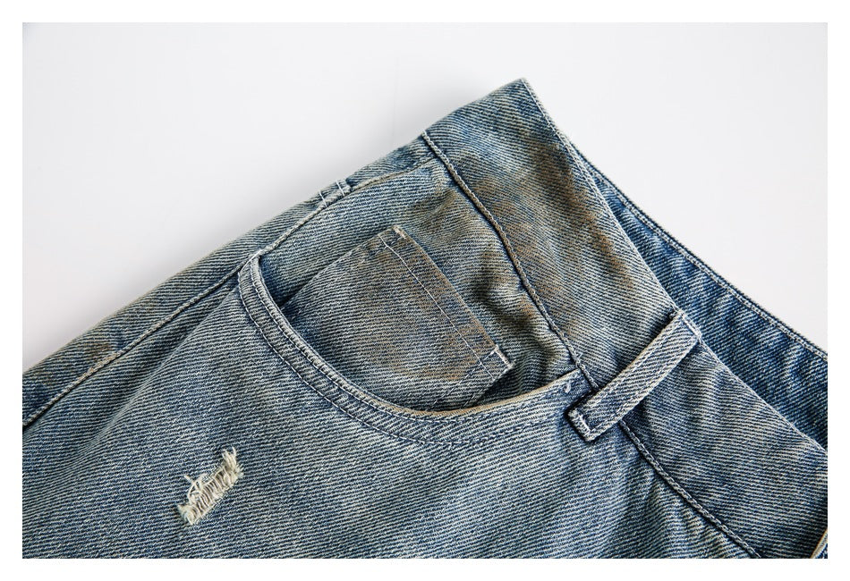 Close-up of a front pocket, belt loop and small embroidered detail on faded blue jeans.