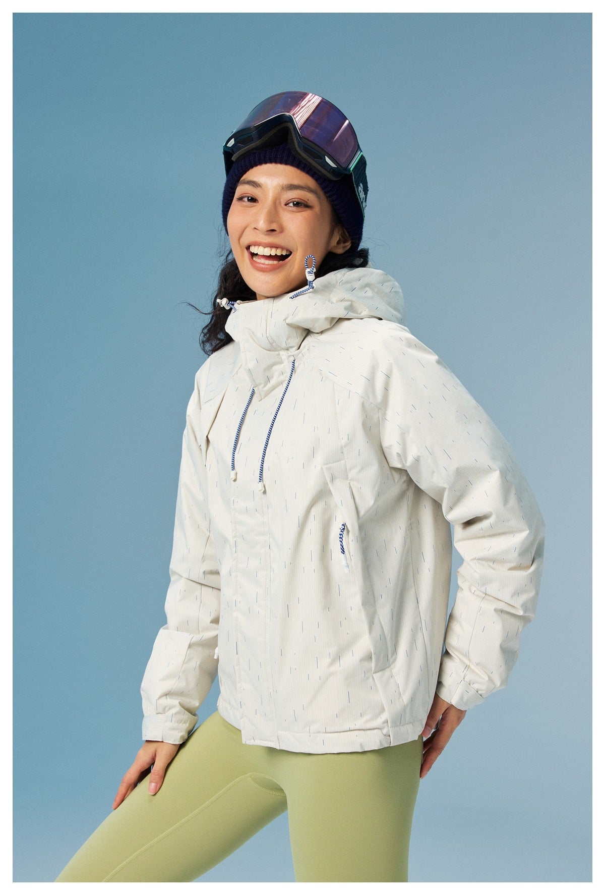 Closer front view of a model in a white patterned hooded jacket with blue drawcords and pale green leggings.