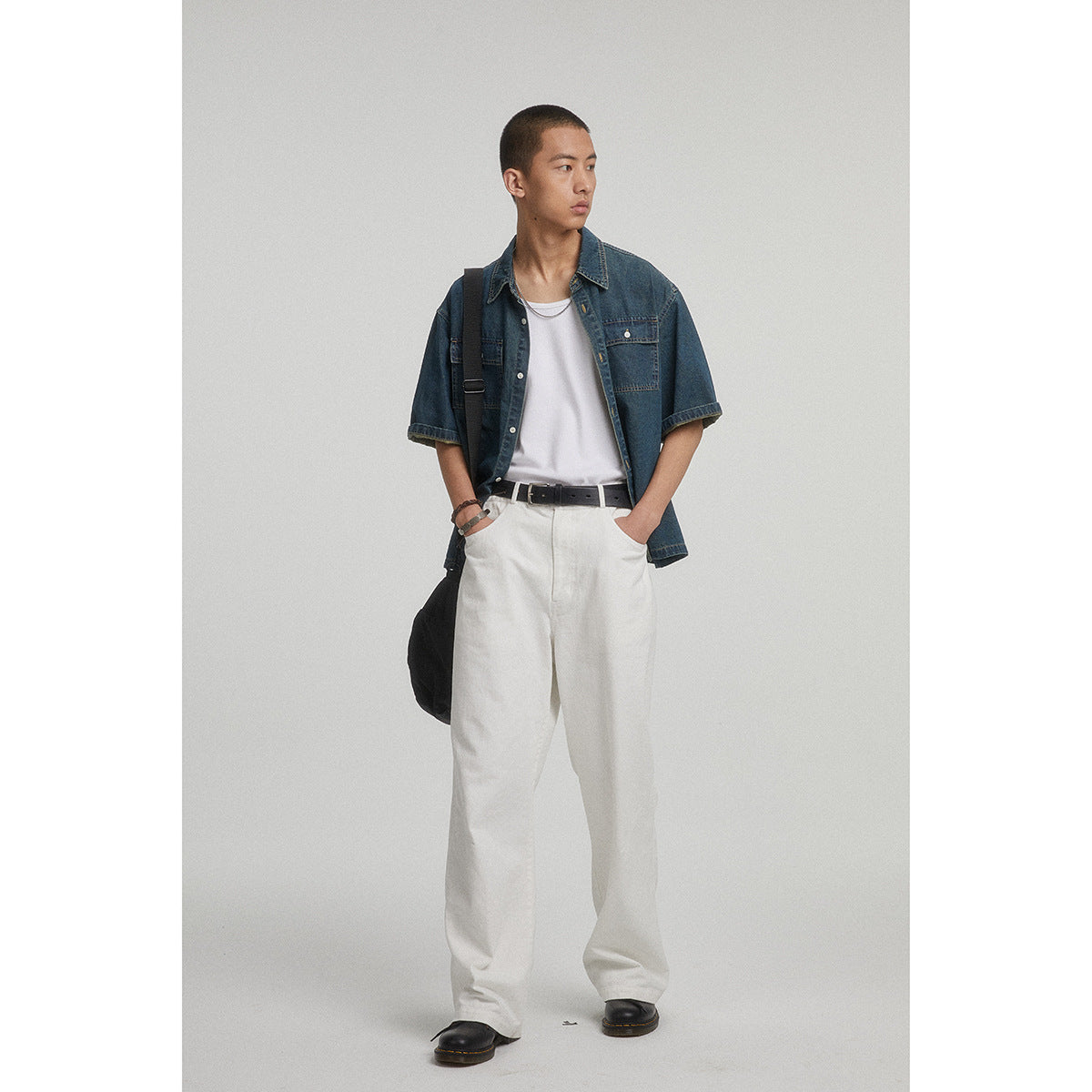 Front view of a model in a dark blue short-sleeve denim shirt with two chest pockets and loose white trousers.
