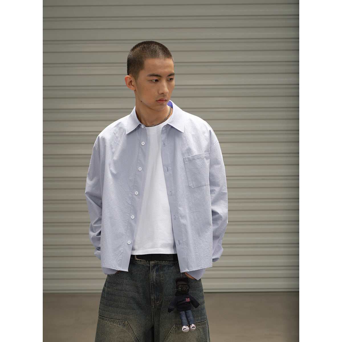 Model wearing an open pale blue button-up shirt with a chest pocket over a white tee.
