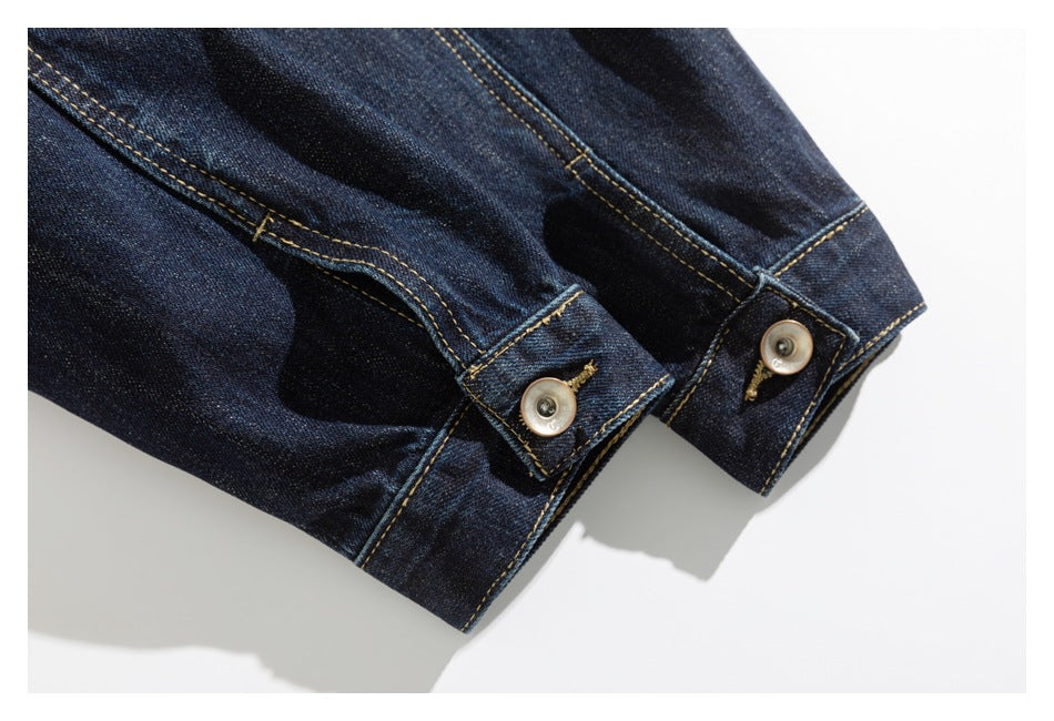 Close-up of two buttoned cuffs on a dark indigo denim jacket with golden stitching.