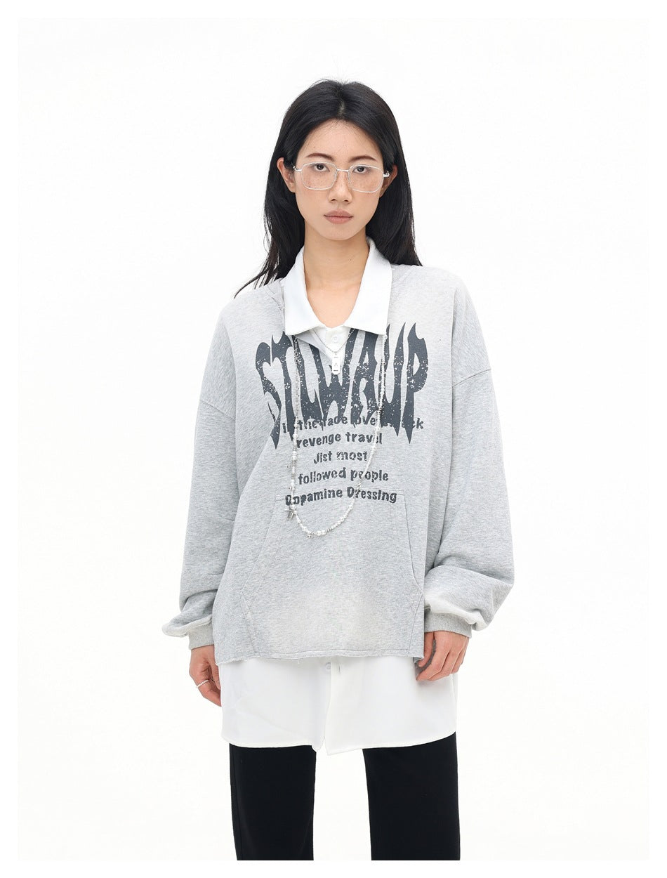 Woman wearing a gray graphic sweatshirt over a white collared shirt with black pants, front view