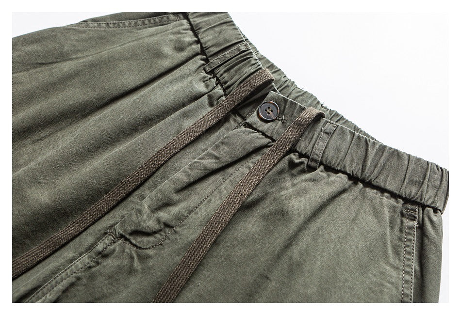 Close-up of olive cargo pants showing the elastic waistband, button closure, belt loops and drawcord.