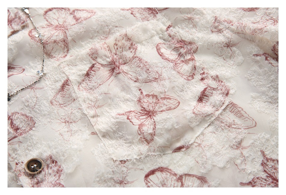 Close-up of ivory fabric with raised white texture, dusty rose butterfly print, and a dark button.