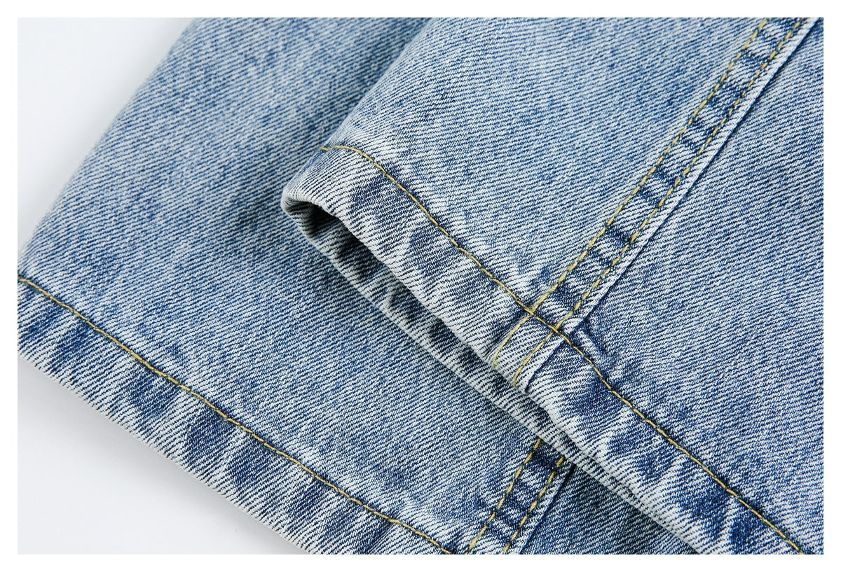 Close-up of light blue denim with a folded edge, intersecting yellow topstitching, and a double-stitched seam.