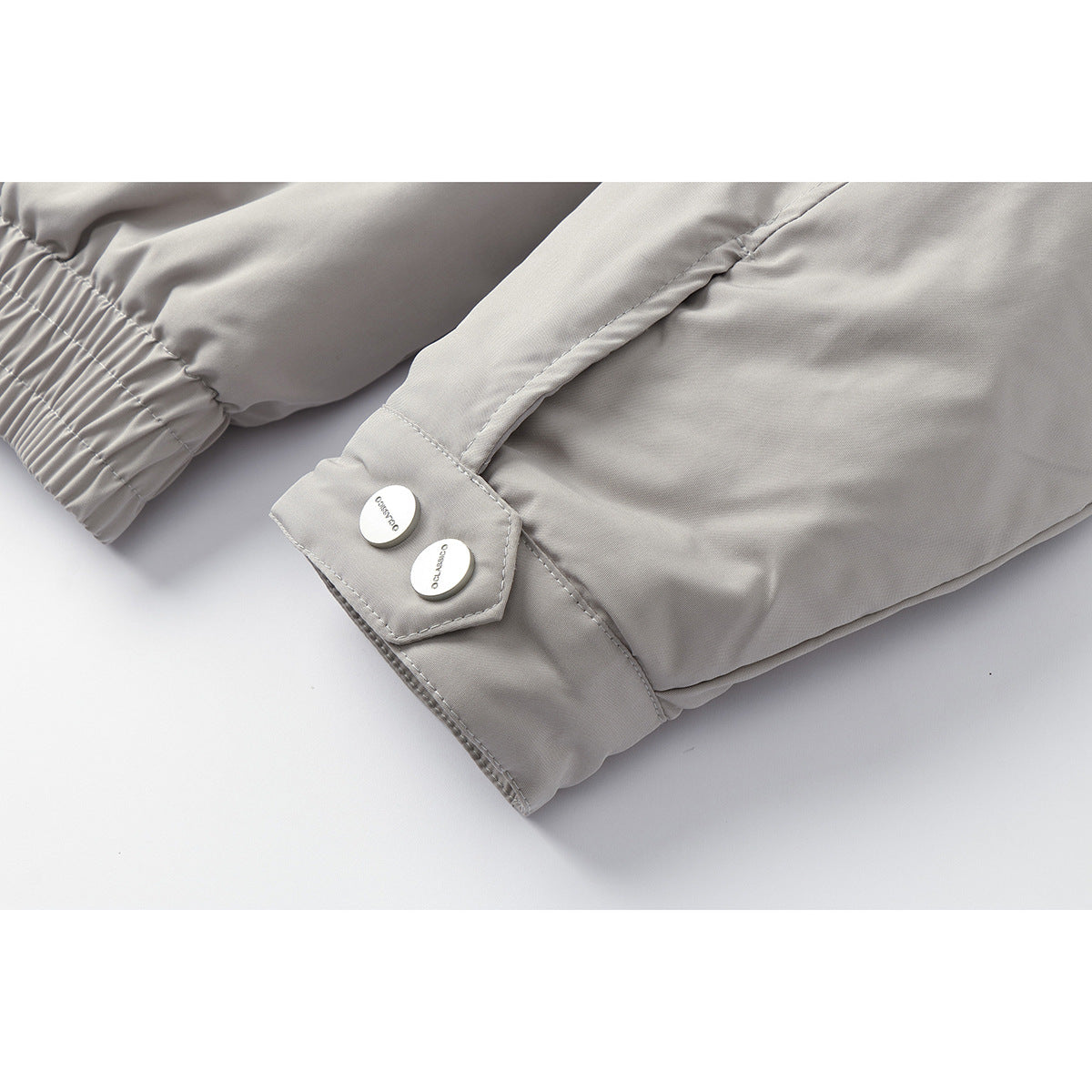 Close-up of a light gray jacket cuff with elastic sleeve gathering and two silver buttons on a tab.
