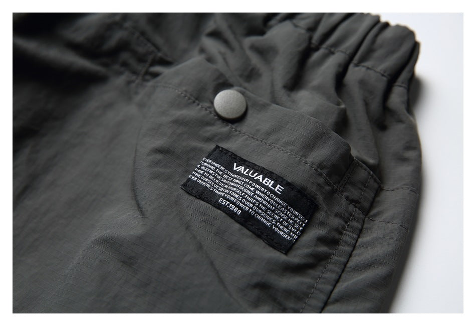 Close-up of a snap-button pocket and sewn black label on charcoal shorts.