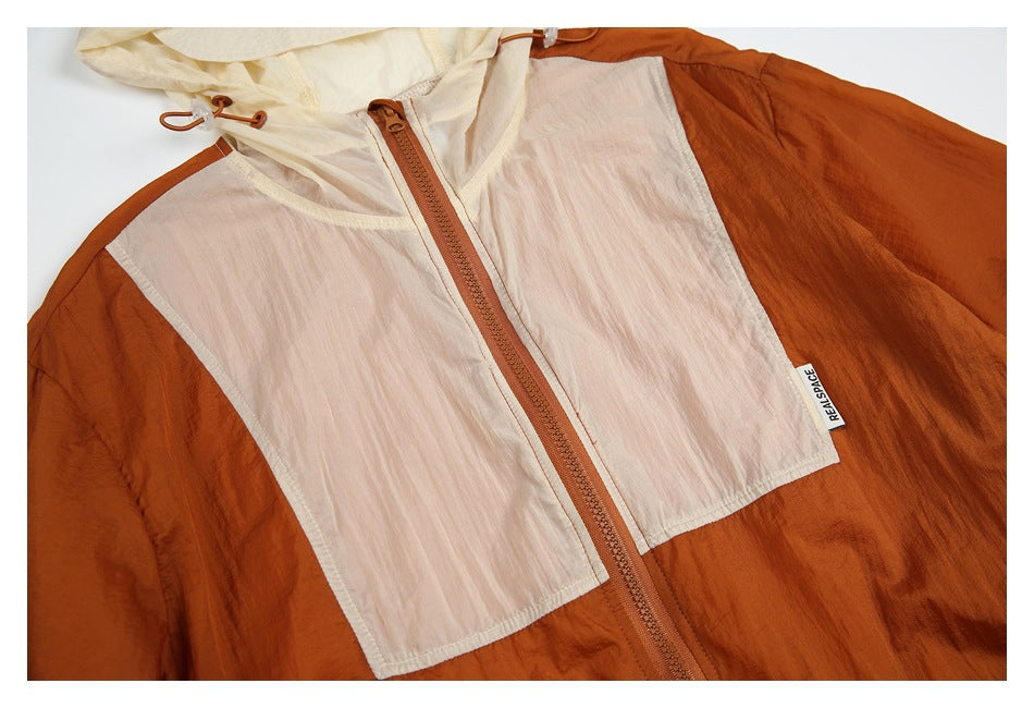 Close-up of a rust jacket front with pale pink panels, cream hood, and a central brown zipper; sewn label visible.