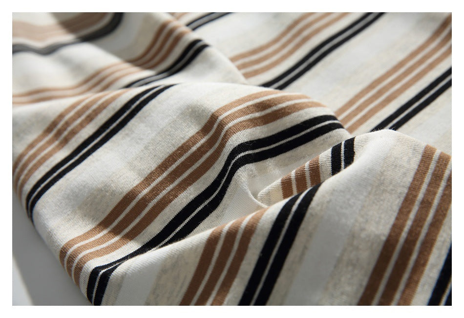Close-up of cream fabric with horizontal black and brown stripes and soft folds.
