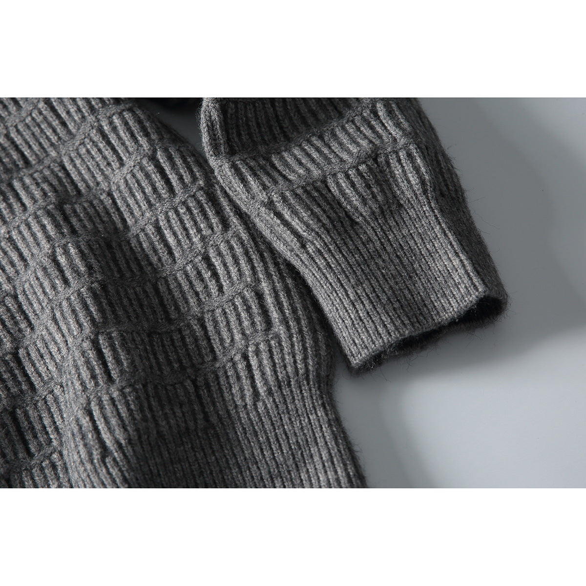 Close-up of a gray textured knit sweater's ribbed cuff and patterned sleeve.