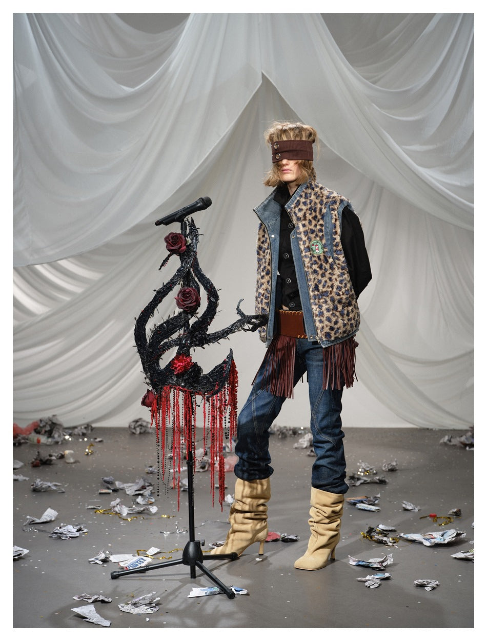 Full-length front view of a model wearing a leopard-print vest with denim trim and burgundy fringe over jeans.