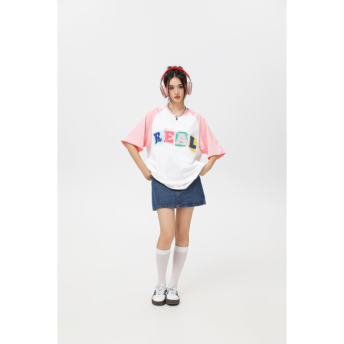 Model wearing a white T-shirt with pink raglan sleeves and colorful REAL lettering, paired with a denim skirt.