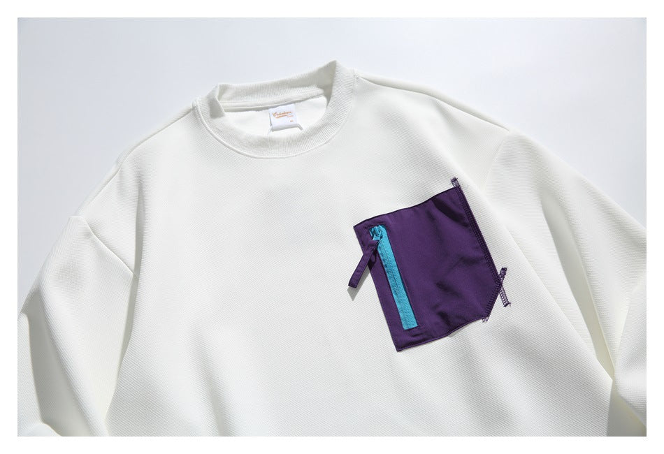 Close view of an ivory crewneck sweatshirt with a purple chest pocket, bright cyan zipper, and purple pull tab.