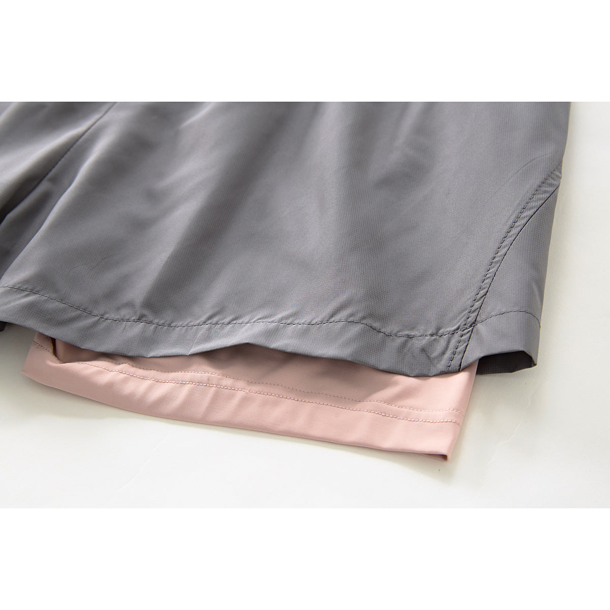 Close-up of the gray shorts' hem, showing a pale pink inner layer and stitched edges.