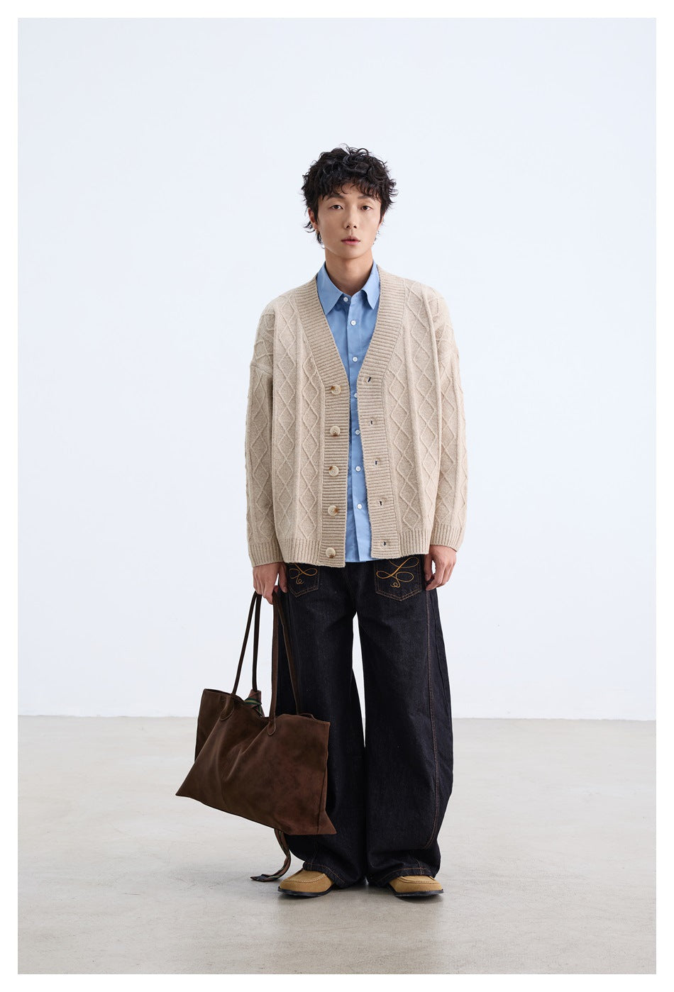 Front view of model wearing a beige diamond-knit button cardigan over a blue shirt and dark jeans.