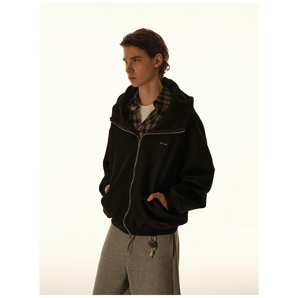 Model wearing a black zip-up hooded jacket over a plaid shirt, shown from the waist up.