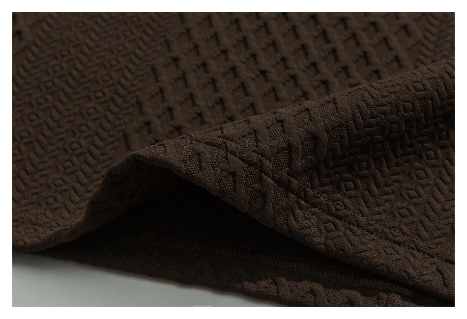 Close-up of dark brown fabric with a raised geometric texture, shown folded to reveal its edge.