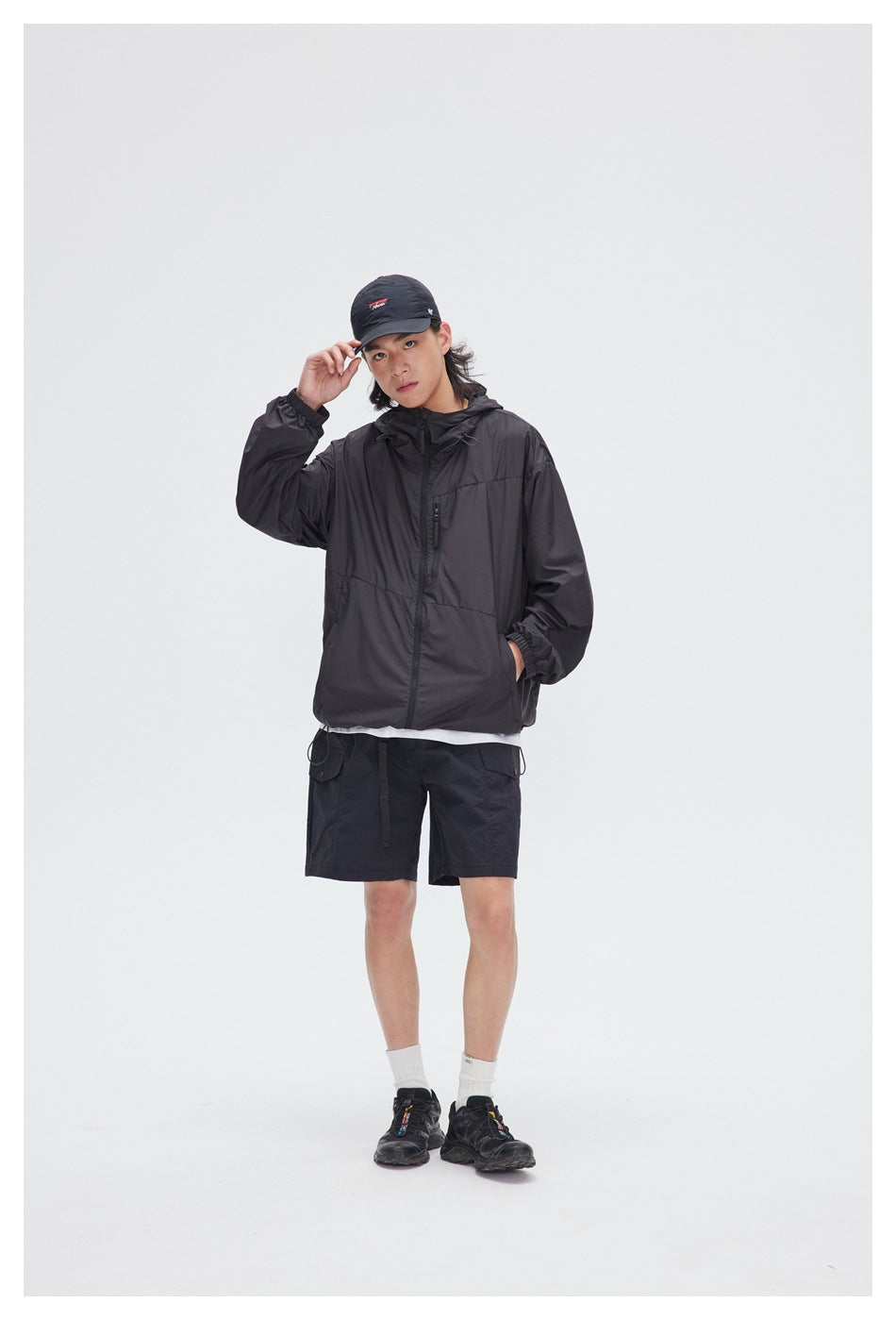 Model wearing a black hooded jacket, black cargo shorts, and a black cap.