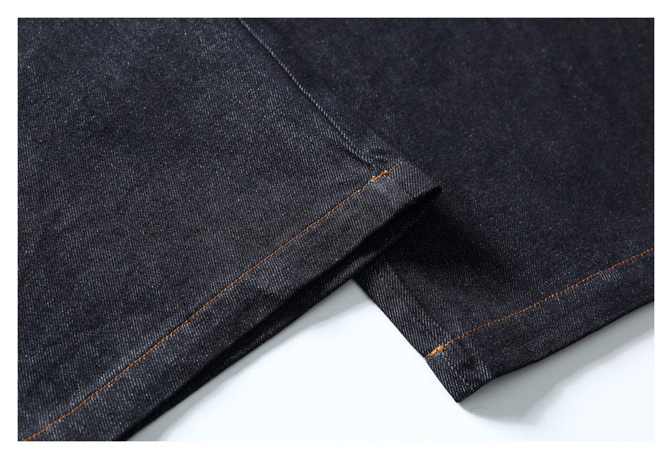 Close-up of dark indigo denim with orange contrast stitching along a folded seam.