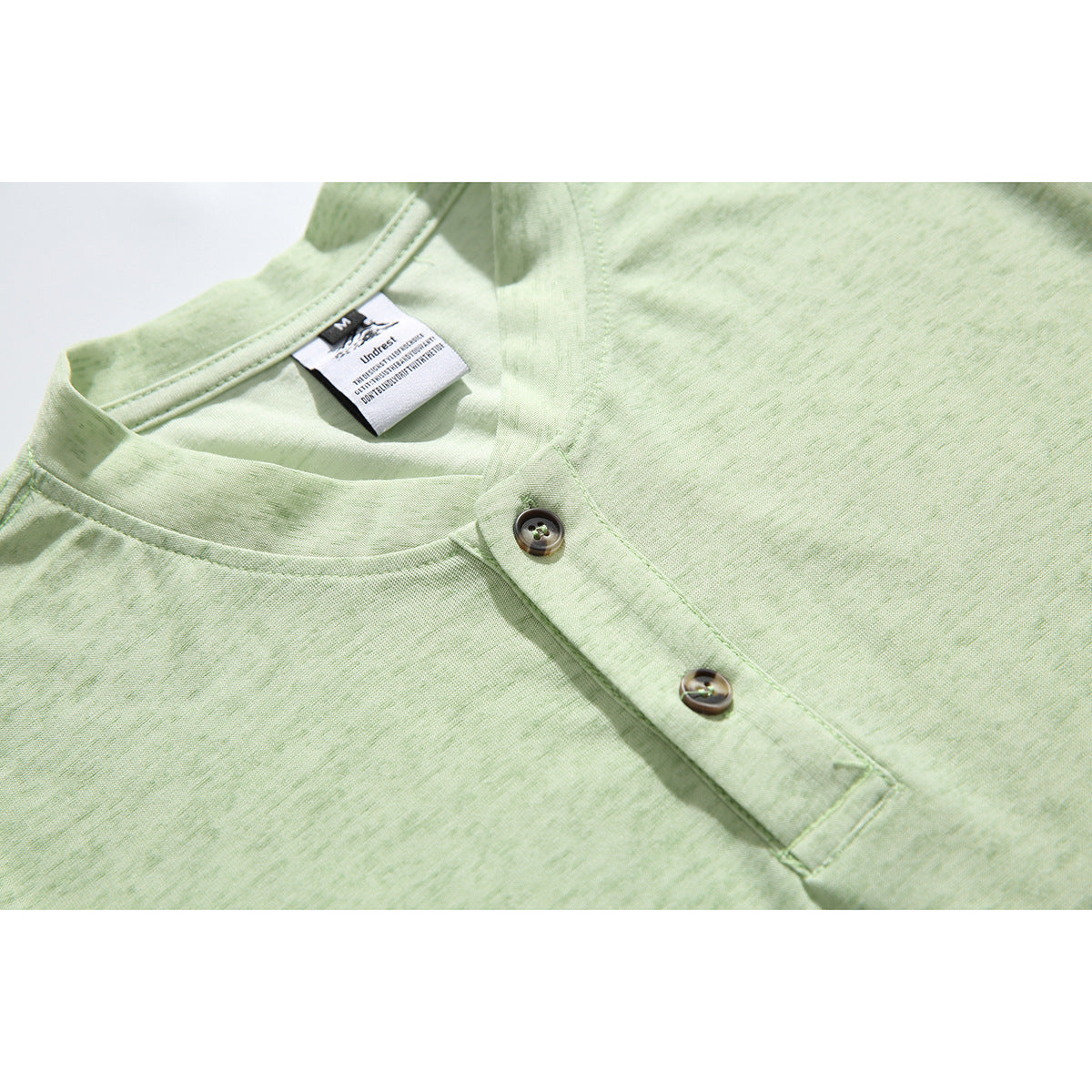 Close-up of a pale green long-sleeve shirt’s band collar and two-button front placket.