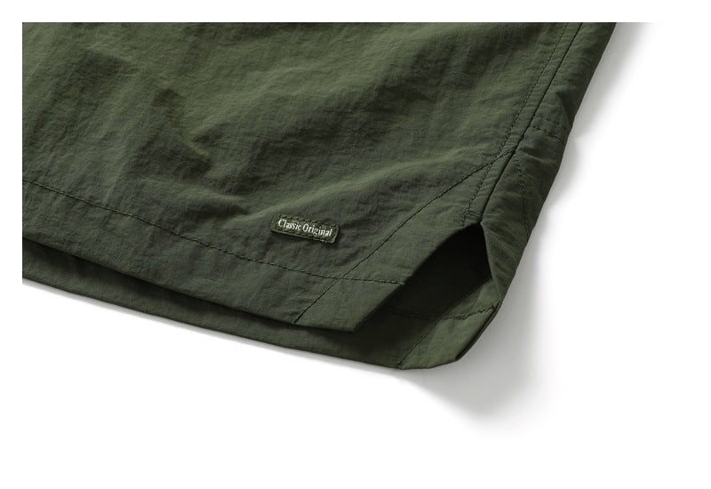 Close-up of a dark olive garment hem with a small sewn “Classic Original” label and angled seam.
